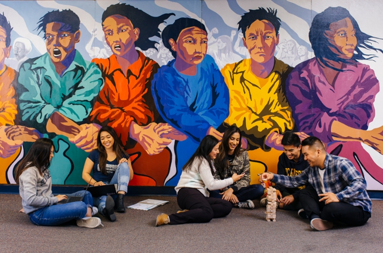 UC Riverside students sitting in front of mural